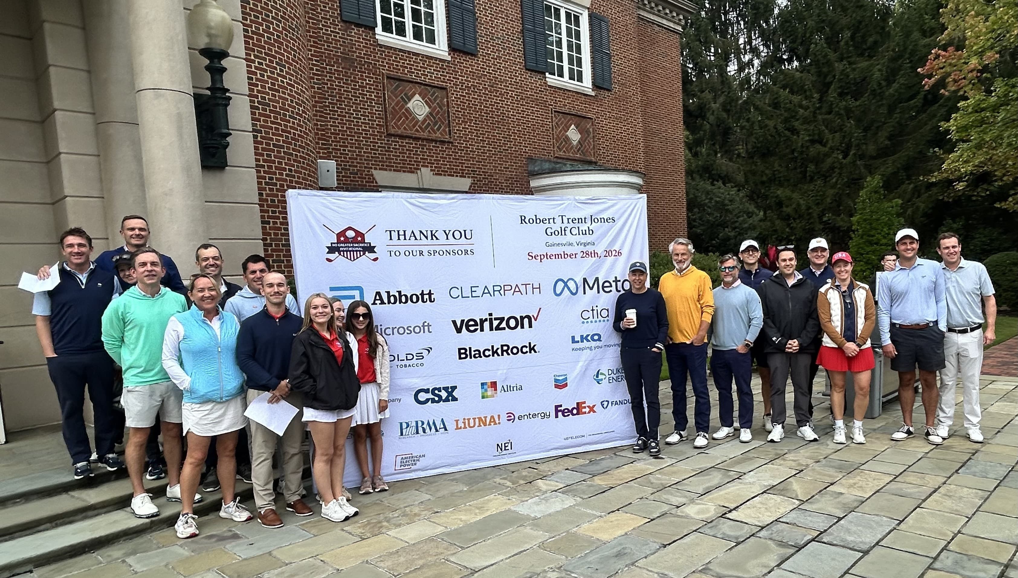 About two dozen golfers pose outside a brick clubhouse around a Thank You to Our Sponsors banner listing Abbott, Clearpath, Meta, Microsoft, Verizon, BlackRock, CSX, Altria, Chevron, FedEx, and other partners.
