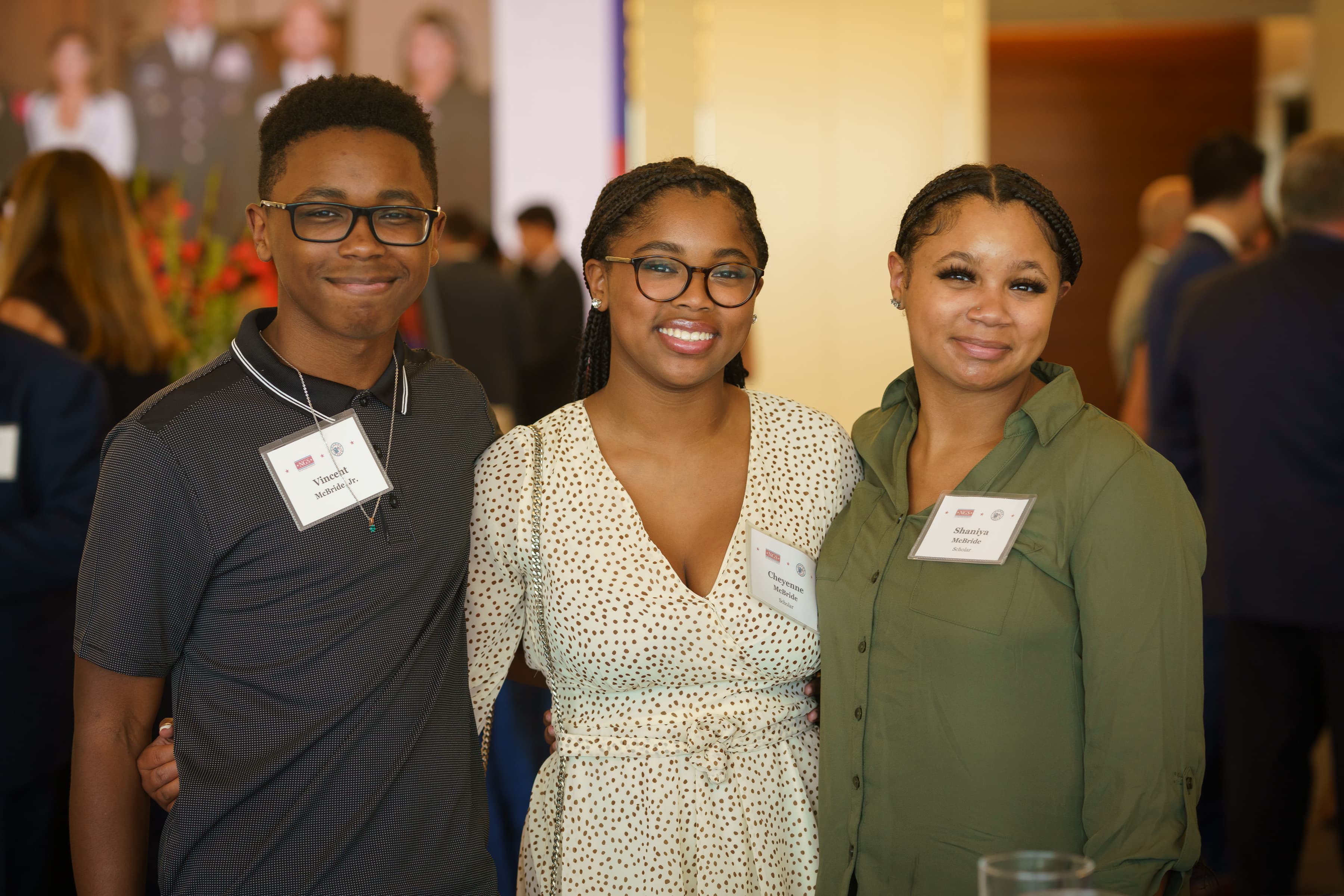 Three young scholars pose together and smile at the 2022 No Greater Sacrifice Freedom Reception gala. All three wear name badges; the young man on the left wears glasses, and the young woman in the center wears a floral dress.