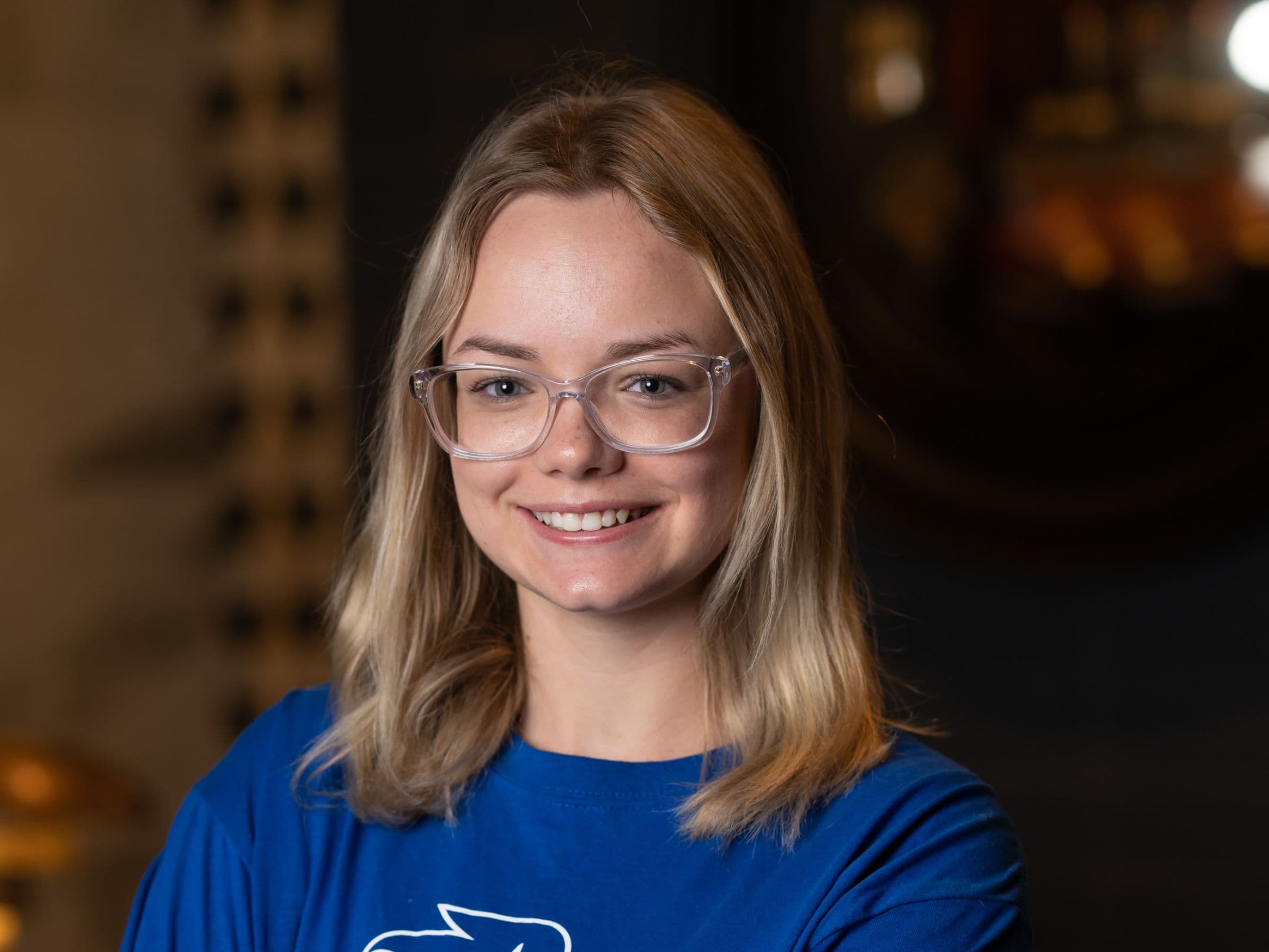 Close portrait of Gracie Edmundson, smiling in clear-framed glasses and a blue T-shirt.